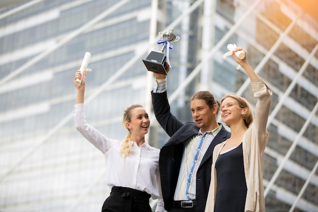 Foto colegas de negócios alegres segurando troféus enquanto estão de pé contra um edifício na cidade