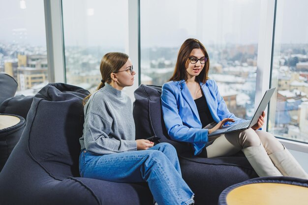 Colegas de negócios com dispositivos digitais encontrando conteúdo de navegação no laptop e discutindo o projeto juntos enquanto estão sentados durante o intervalo do trabalho Discussão corporativa de trabalho em equipe