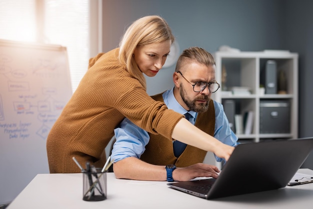 Colegas de negócios focados usando laptop moderno durante reunião no escritório Parceiros masculinos e femininos discutindo projeto comum Cooperação e conceito de tecnologia