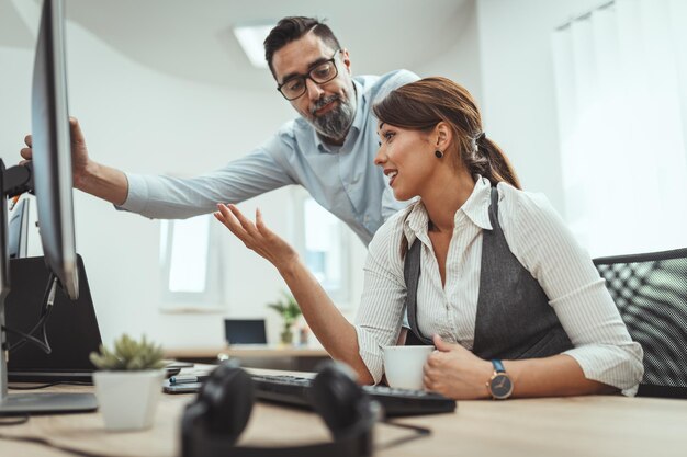 Colegas de negócios jovens estão analisando o projeto e trabalhando em um computador no escritório enquanto a mulher bebe café.