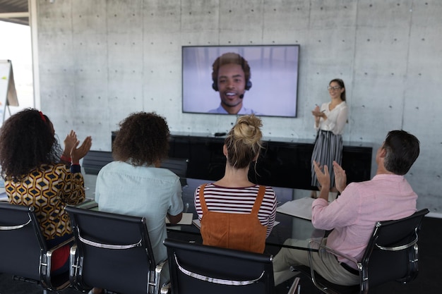 Foto colegas de trabalho aplaudindo enquanto assistem a uma chamada de vídeo em uma sala de conferências