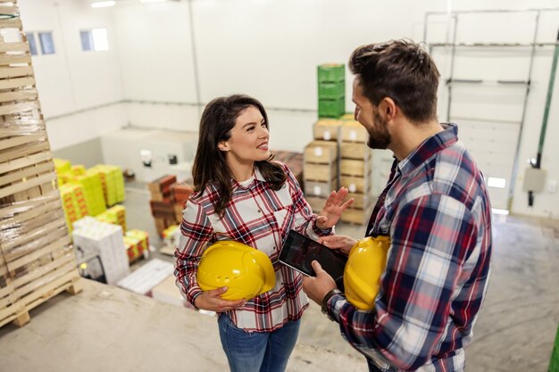 Foto colegas de trabalho em camisas xadrez e com um capacete amarelo protetor falam sobre o status do trabalho