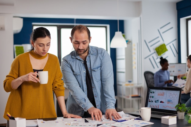 Colegas de trabalho multiétnicas discutindo em gráficos de estatísticas do local de trabalho para obter instruções com a gerência. Equipe diversificada de executivos que analisam relatórios financeiros da empresa a partir do computador. Arranque corp com sucesso