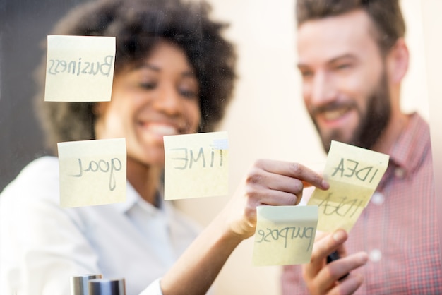 Colegas de trabalho multiétnicas trabalhando em conjunto com adesivos na porta transparente do escritório