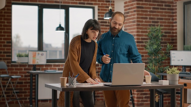 Colegas de trabalho olhando para a tela do laptop e papéis gráficos para trabalhar no planejamento de projetos e estratégia de negócios. Colegas usando gadget para projetar apresentação de marketing e análise de dados.