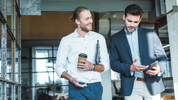 Colegas de trabalho sorridentes conversando enquanto caminham pelo corredor