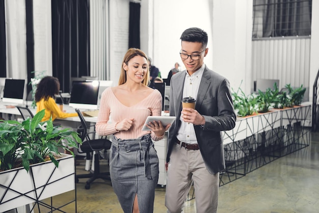 Colegas de trabalho sorridentes usando tablet digital e entrando no escritório