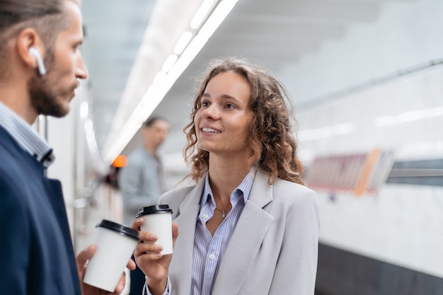 Colegas de trabalho tomando café para viagem em pé na plataforma do metrô