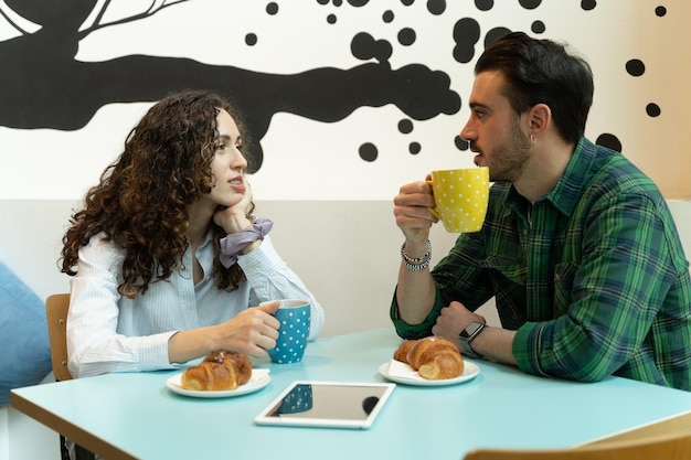 Colegas discutem trabalho tomando café, um tablet digital e croissants na mesa