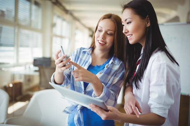 Colegas discutiendo con tableta digital y teléfono móvil en la oficina creativa