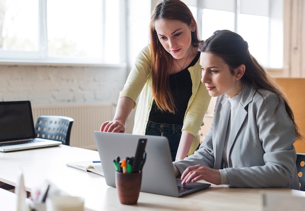 Colegas femeninos jovenes que trabajan en el ordenador portátil en oficina