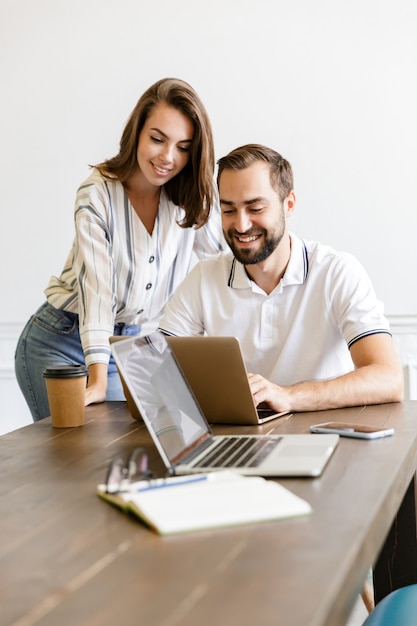 colegas de la joven pareja sonriente feliz trabajan con la computadora portátil en el interior de la oficina hablando entre sí.