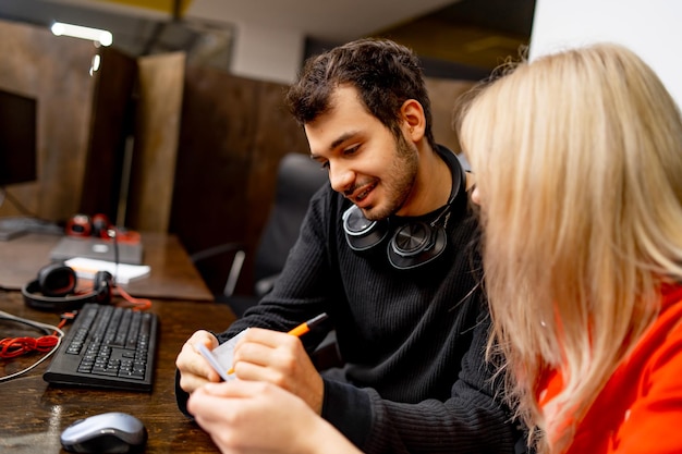 Colegas masculinos e femininos estão discutindo algo no escritório moderno Desenvolvedores de software estão sentados à mesa com o conceito de plano de negócios de computador