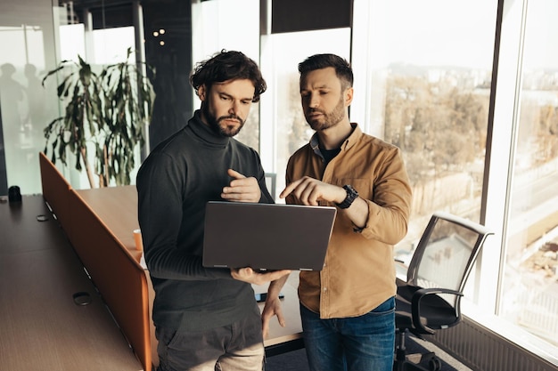 Colegas masculinos trabajando juntos usando una computadora moderna en una oficina de espacios abiertos