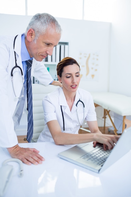 Colegas médicas concentradas discutindo e trabalhando com laptop