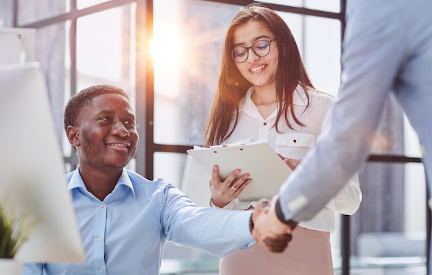 Colegas multirraciais alegres discutindo projeto de inicialização e sorrindo durante o dia de trabalho no interior do escritório