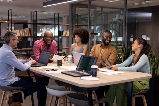 Colegas multirraciales sonrientes discutiendo durante una reunión en un lugar de trabajo moderno