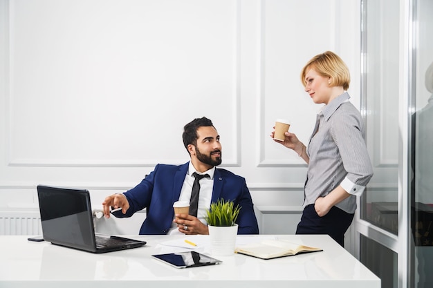 Colegas de negocios exitosos que sostienen tazas de trabajo de café con una computadora portátil en el interior de la oficina blanca