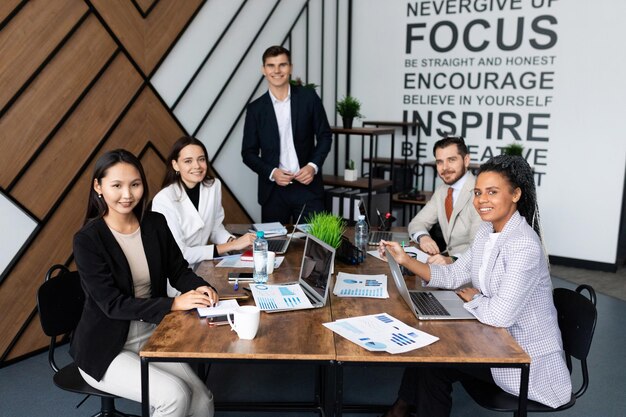 Colegas en la oficina en una gran mesa de trabajo miran la cámara