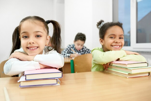 Colegas que levantam na mesa na sala de aula, inclinando-se em livros.