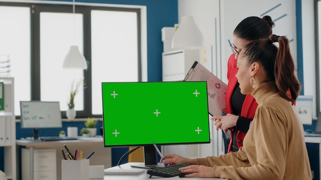 Colegas que trabalham com tela verde em exibição, usando fundo de croma e modelo de simulação isolado no escritório de inicialização. Mulheres com aplicativo de espaço de cópia chromakey no monitor do computador.