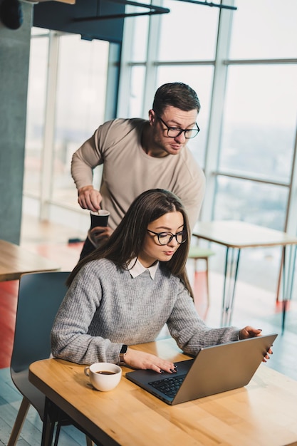 Colegas se comunicam enquanto trabalham com um laptop no escritório Dois trabalhadores em um espaço de trabalho moderno Dois jovens empresários estão sentados juntos em uma mesa