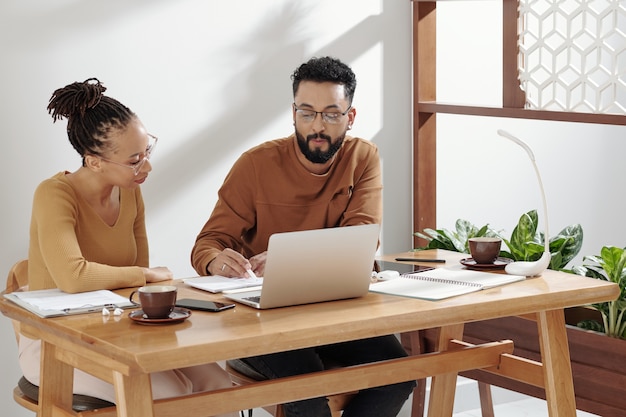 Foto colegas sentados à mesa do escritório com o laptop aberto e trabalhando no plano de negócios