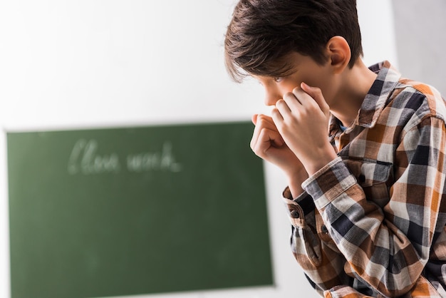 Colegial acosado y deprimido que cubre la cara en el aula