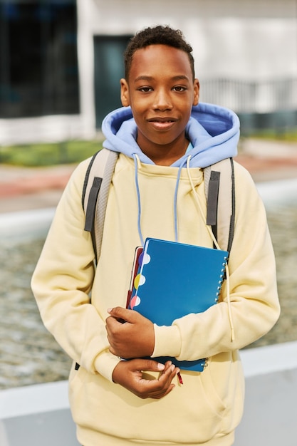 Colegial afroamericano sonriente con cuadernos y mochila