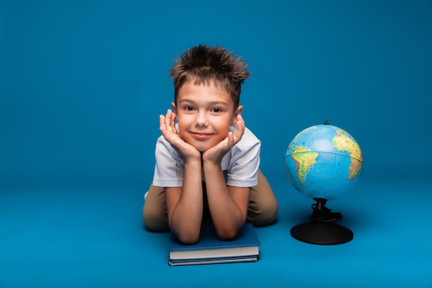 El colegial alegre se sienta en un fondo azul con una mochila y un concepto de educación del globo