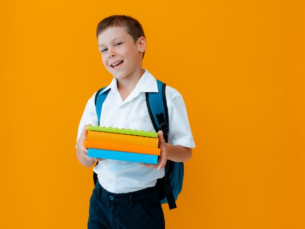 Colegial alegre sonriente sobre fondo amarillo. Un niño con mochila, libros y cuadernos.