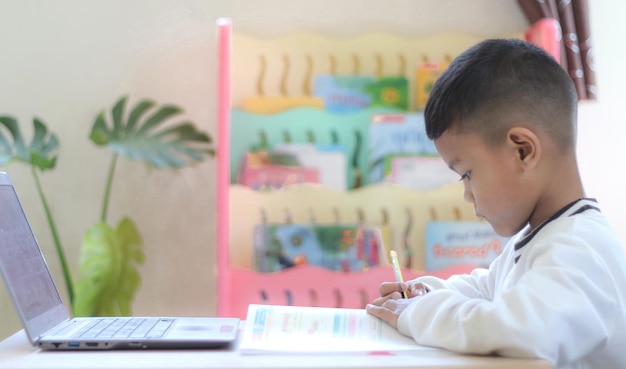 Colegial asiático haciendo su tarea con una computadora portátil en casa Los niños usan aparatos para estudiar Educación y aprendizaje a distancia para niños Educación en el hogar durante la cuarentena Quédese en casa