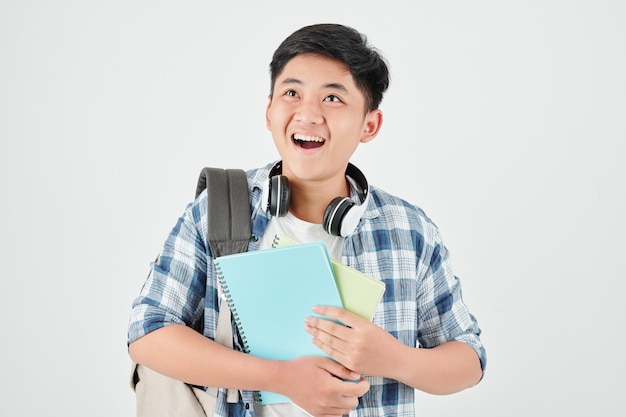 Colegial asiático sorprendido con libros de texto en las manos mirando hacia arriba y abriendo la boca de la emoción