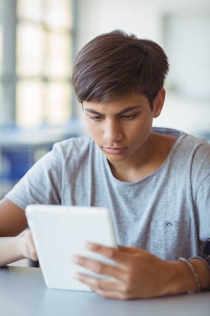 El colegial atento con tableta digital en el aula