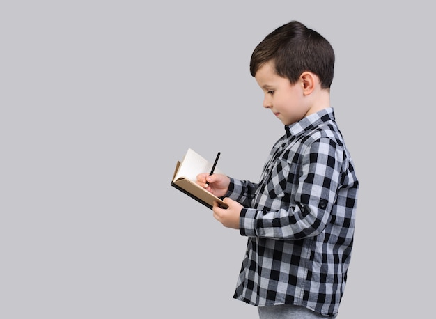 Un colegial con una camisa gris escribe en un cuaderno