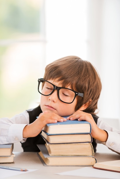 Colegial cansado. Lindo joven durmiendo mientras está sentado en la mesa e inclinando su rostro en la pila de libros