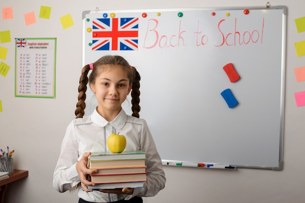 Foto colegial com uma pilha de livros perto do quadro