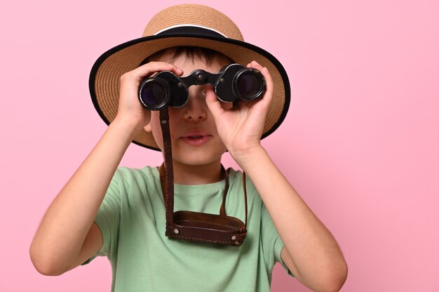 Colegial curioso en verano sombrero de paja mirando a través de binoculares antiguos