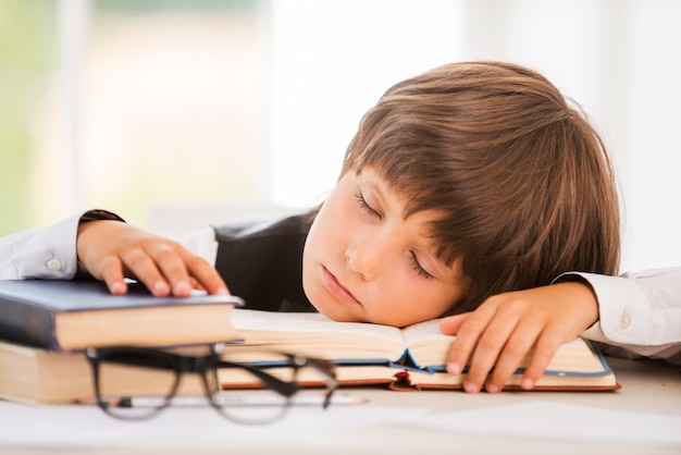 Foto colegial durmiendo. cute little boy durmiendo mientras está sentado en la mesa y apoyando su rostro en el escritorio