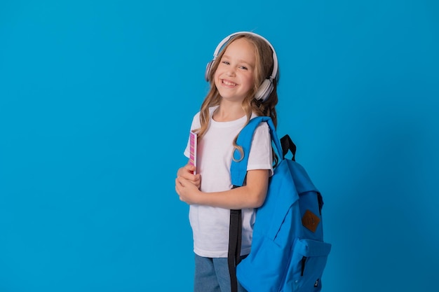 colegial em uma camiseta branca, fones de ouvido, com uma mochila no ombro e um caderno listrado