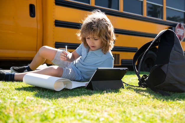 El colegial escribiendo al aire libre en el parque escolar y haciendo los deberes en el autobús escolar