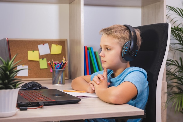 Colegial en estudios de auriculares en casa con computadora portátil Aprendizaje en casa