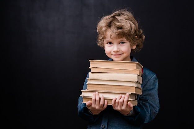 Colegial exitoso sosteniendo la pila de libros contra el espacio negro