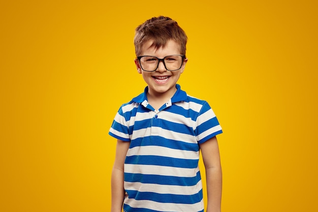 Foto colegial feliz en polo de rayas azules y gafas sonriendo aislado sobre fondo amarillo
