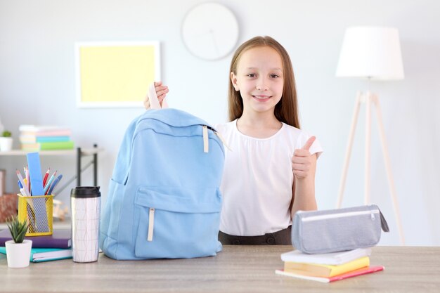 Colegial fofa e alegre colocando papel de carta em uma mochila