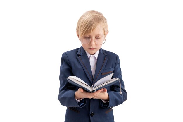 Colegial con gafas grandes mira el libro Niño rubio en uniforme escolar lee el libro de texto aislado sobre fondo blanco.