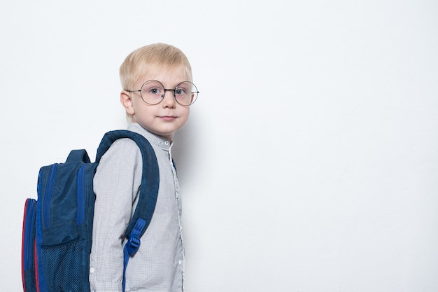 El colegial con gafas y mochila sobre superficie blanca