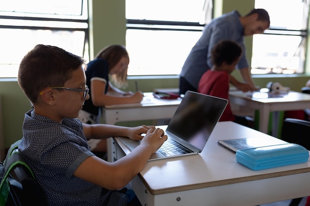 Un colegial con gafas sentado en un escritorio usando una computadora portátil