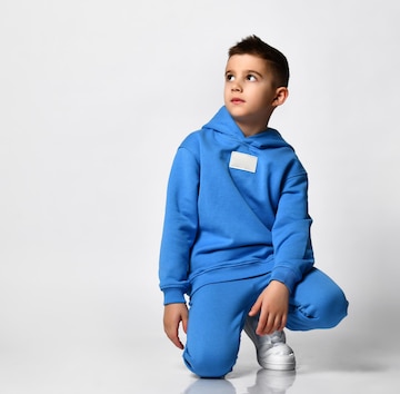Un colegial genial con ropa deportiva azul brillante moda se sienta en un fondo blanco el niño mira espacio vacío para el texto el concepto de ropa infantil y estilo infantil | Foto Premium