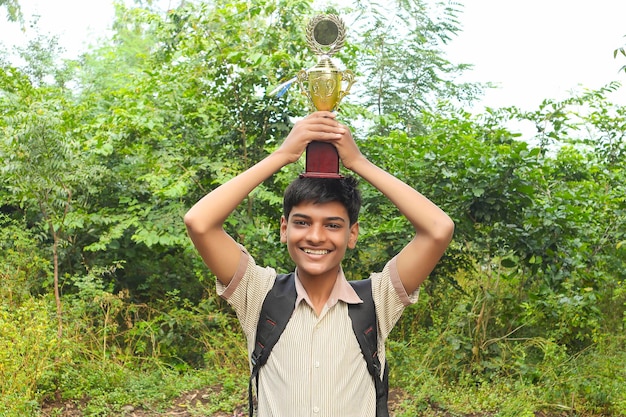 Colegial inteligente levantando su trofeo como ganador en la competencia escolar